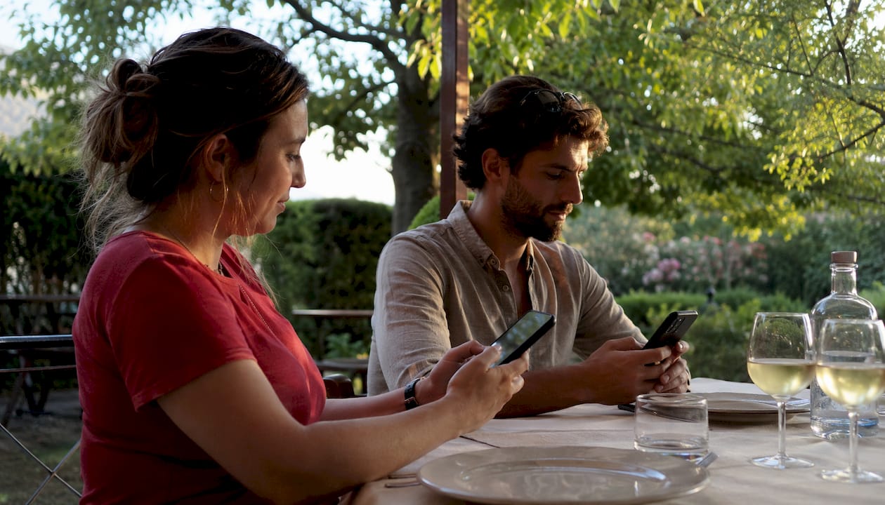 Al tavolo di un ristorante all’aperto, i clienti consultano il menù digitale direttamente dallo smartphone.