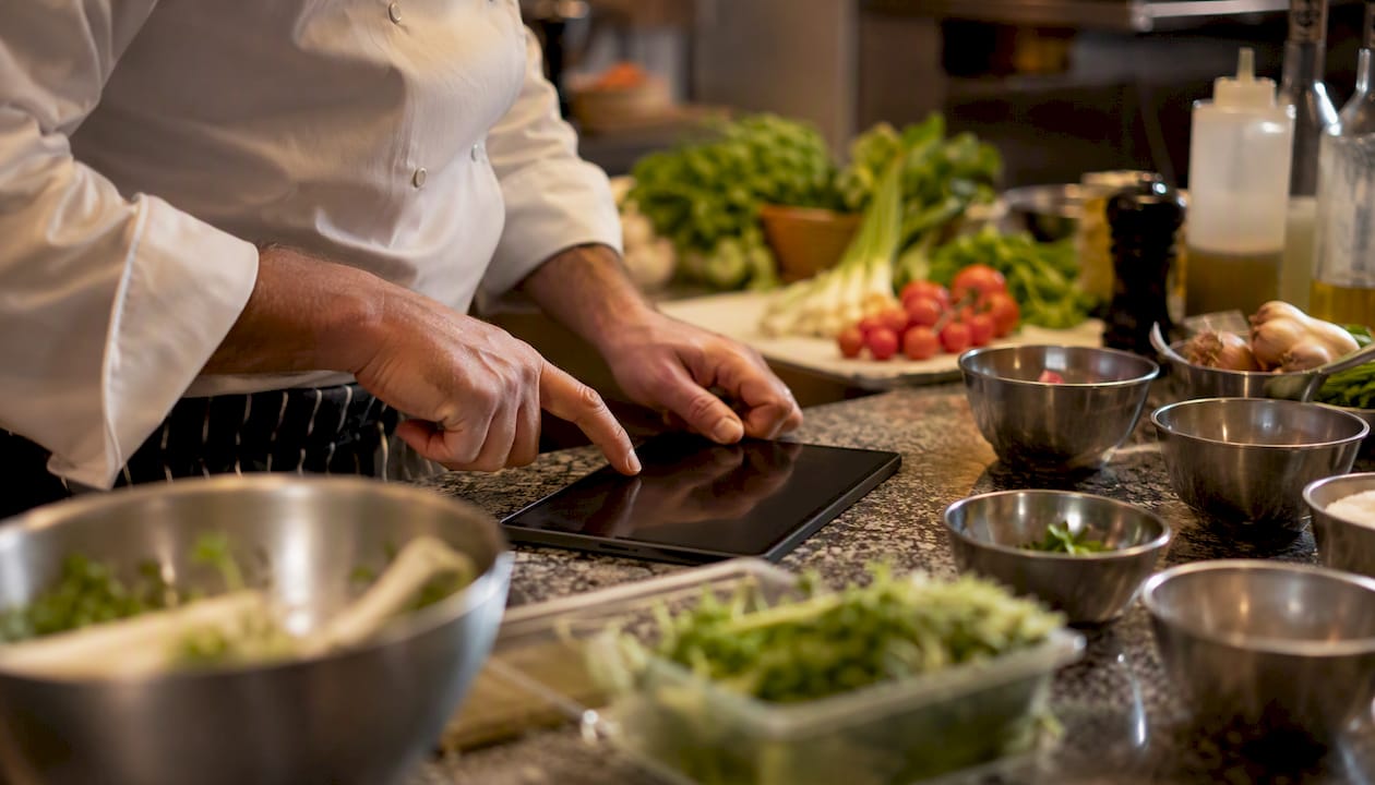 Le mani dello chef che regolano le dosi degli ingredienti direttamente sul tablet
